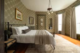 Sunny, historic bedroom with iron bed, high ceilings and tall windows
